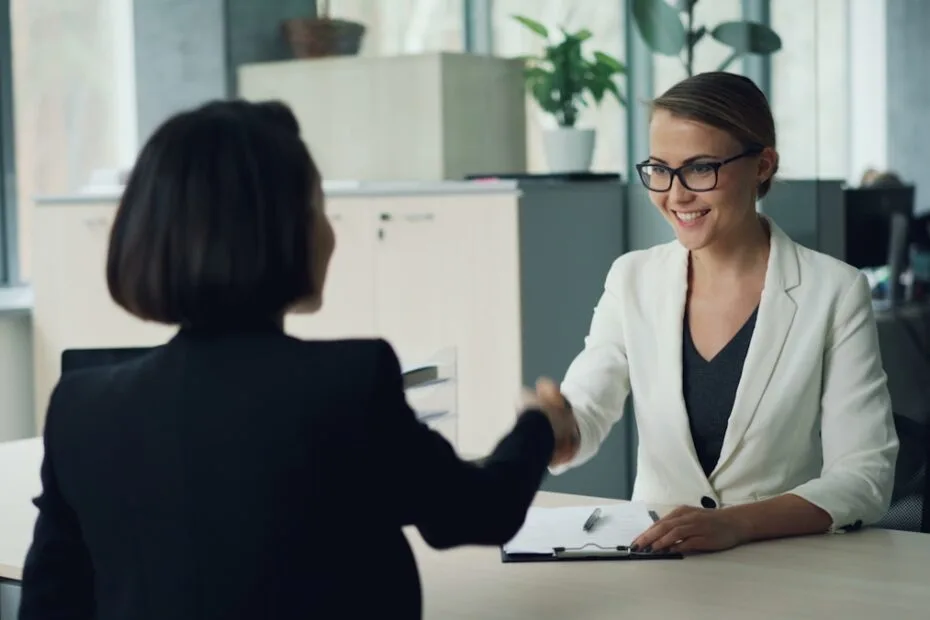 Twee vrouwen schudden handen over bureau tijdens werving en selectie